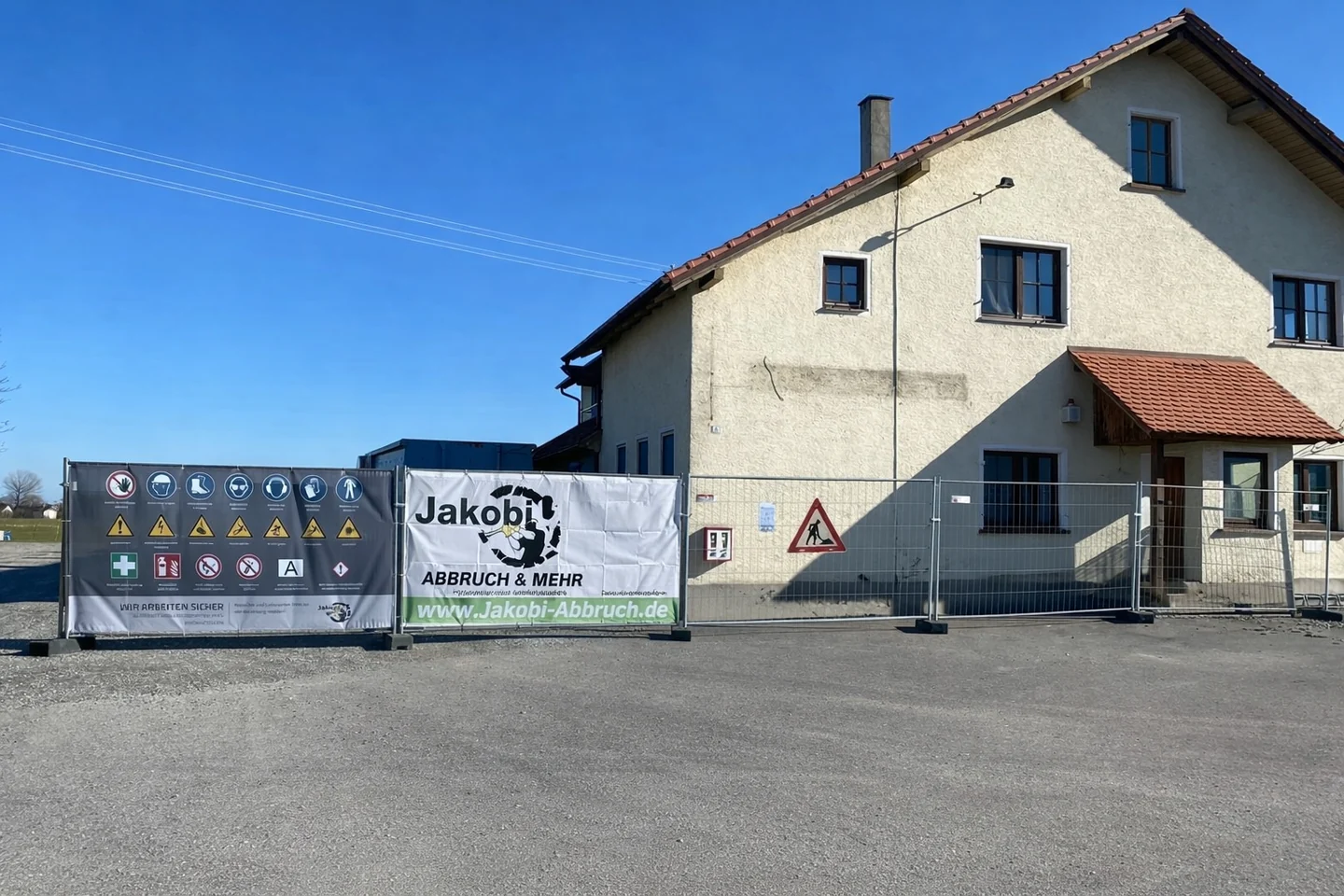 Gebäude mit JAKOBI-Werbebanner und Sicherheitshinweisen am Bauzaun