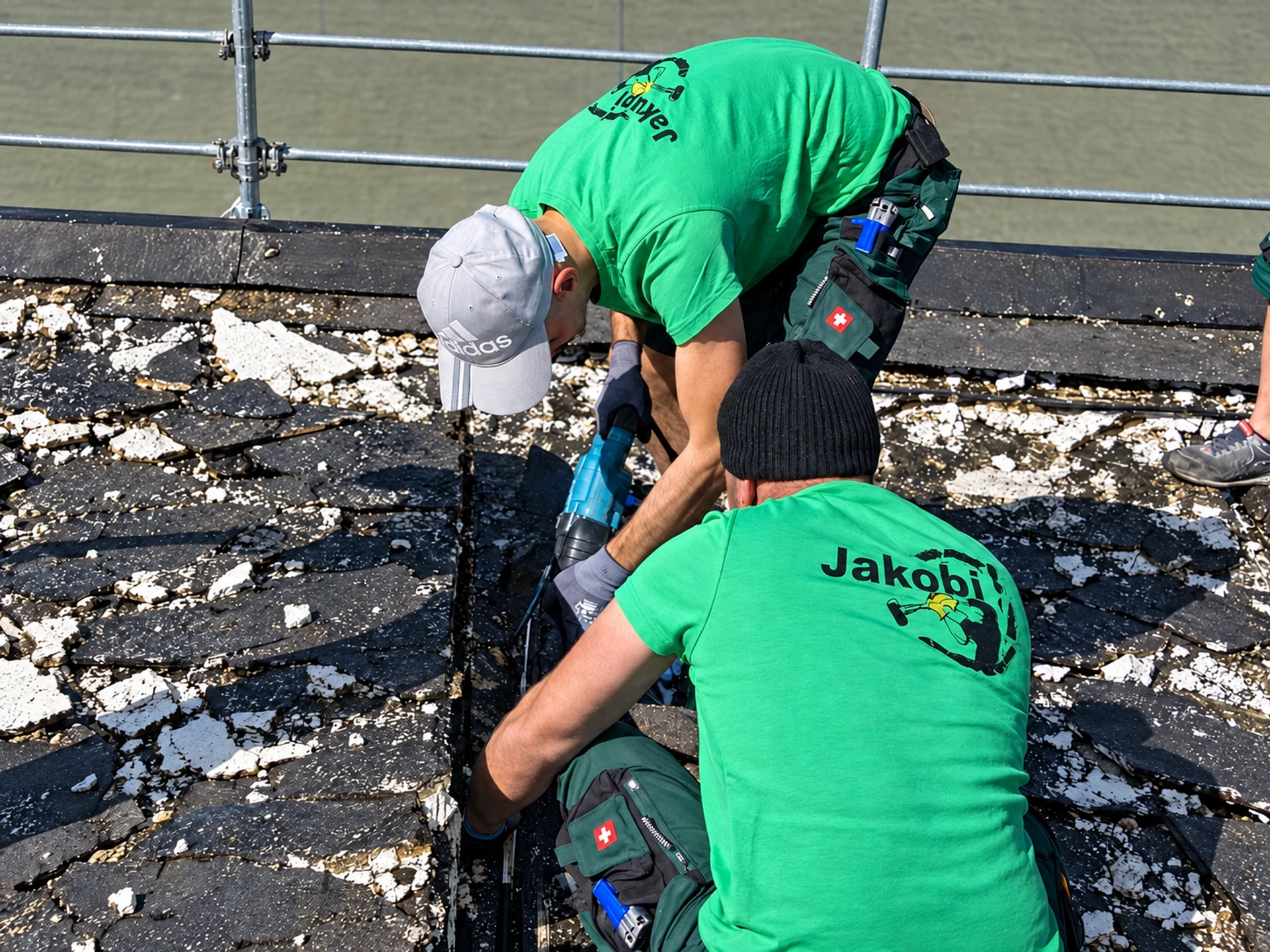 Zwei JAKOBI-Mitarbeiter in grünen Firmen-Shirts beim Rückbau eines Flachdachs
